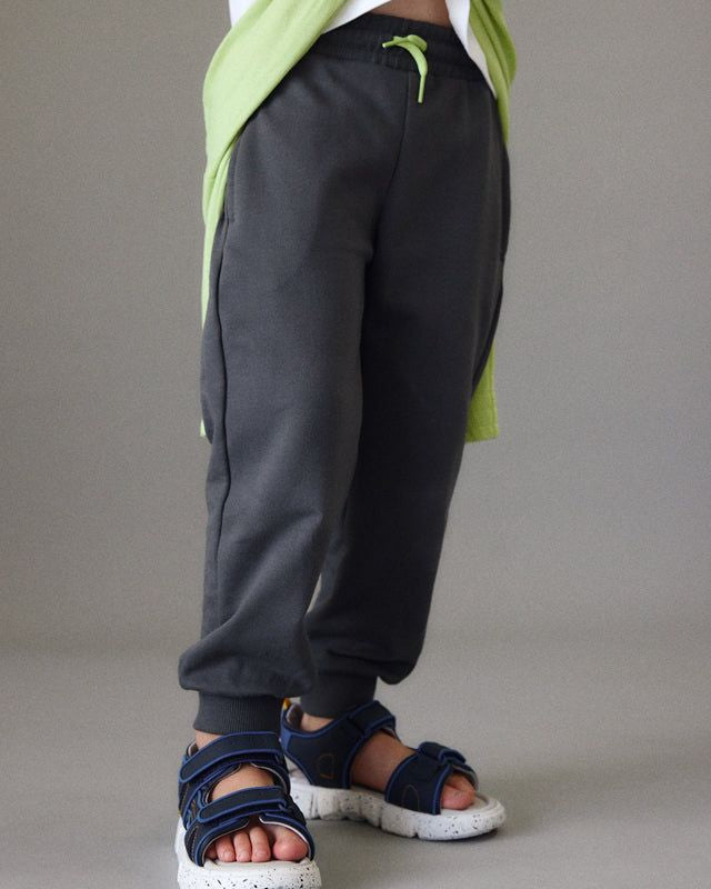 Bambino con pantaloni sportivi in grigio e sandali in blu