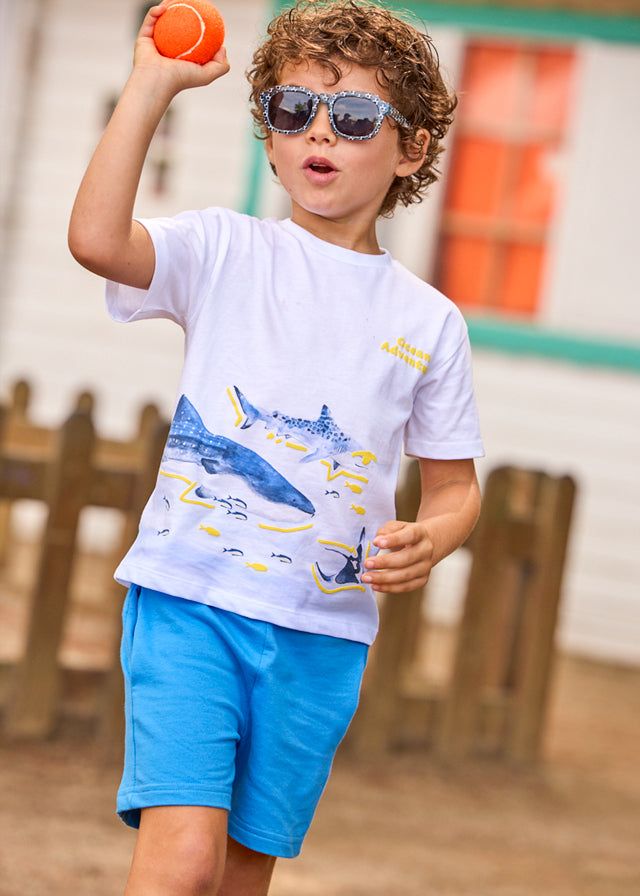 Bambino con occhiali da sole, maglietta con grafica squali e pantaloncini blu, abbigliamento estivo bambino